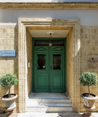 The green double doors of Centrum Hotel on Pasikratous Street, framed in limestone with potted olive trees